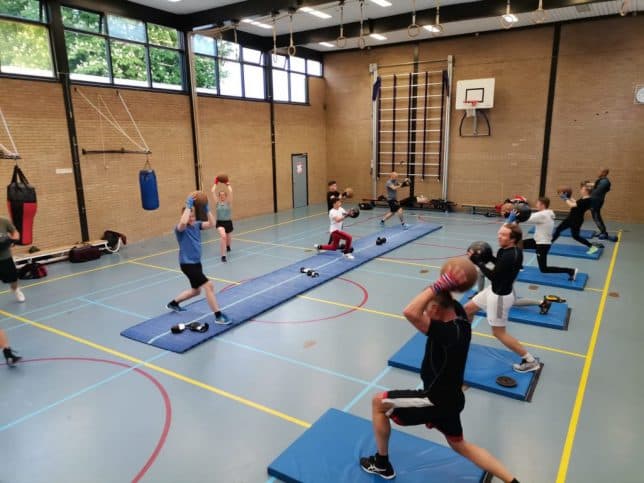 Leden doen een warming-up op matten in de gymzaal